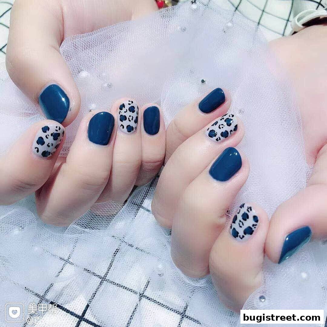 Close-up of hands with dark blue and leopard print nail art.