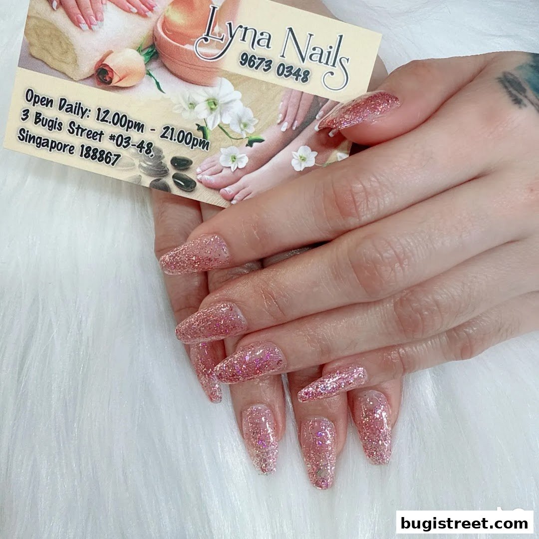 A close-up of hands with sparkling pink glitter acrylic nails, next to a business card.