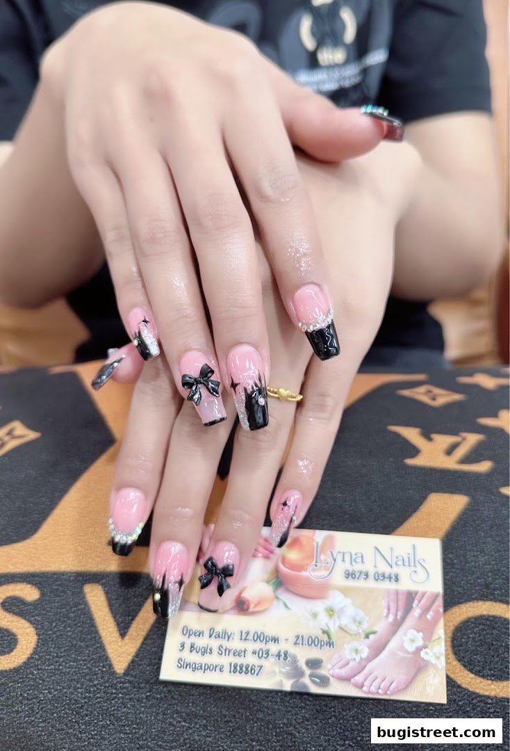 Close-up of hands with elaborate pink and black nails featuring bows and rhinestones.