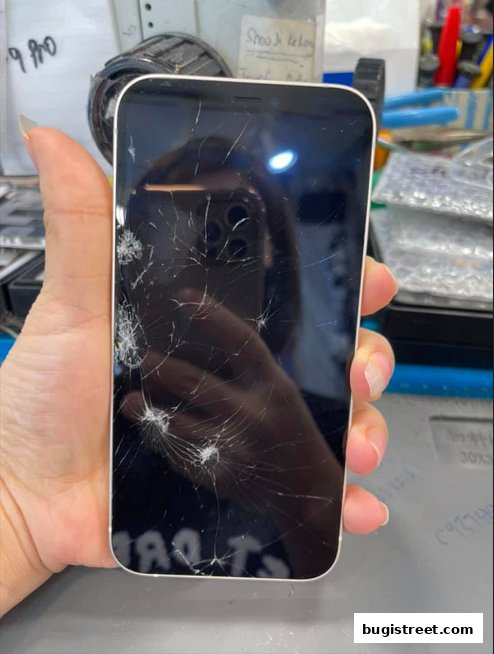 A hand holds a smartphone with a severely cracked screen, ready for repair.