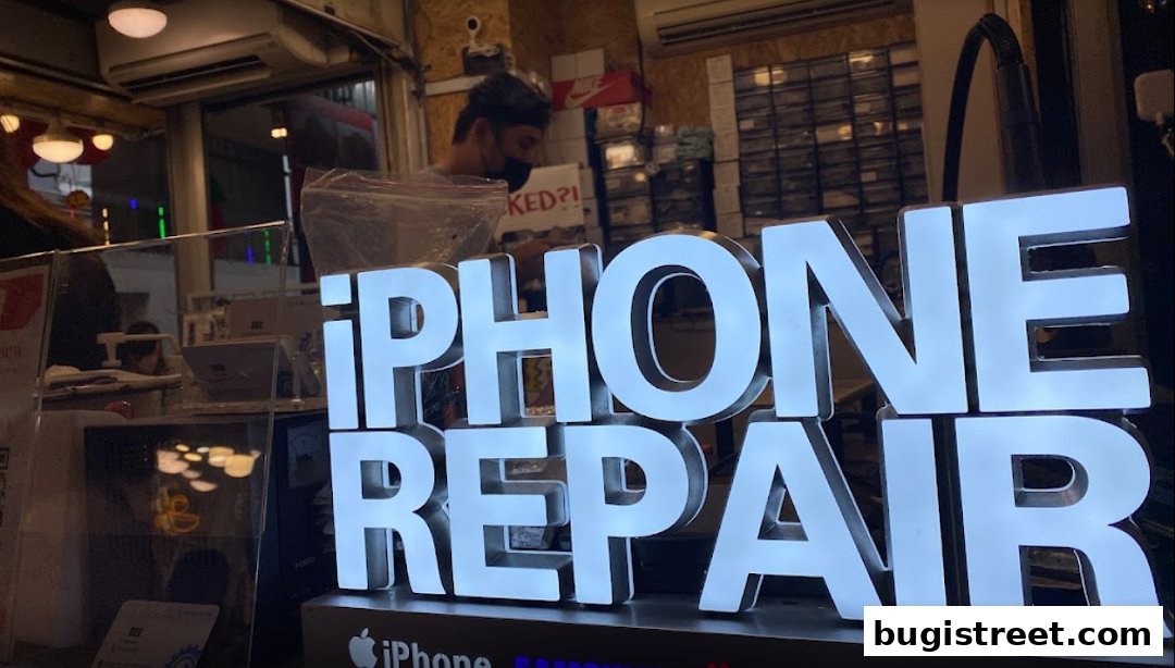 A lit sign for 'iPhone Repair' inside a shop with a technician working.