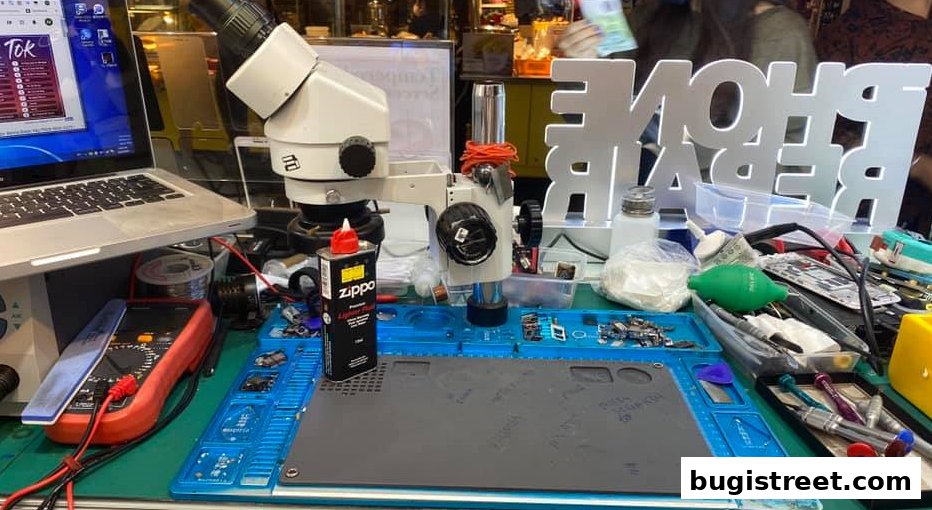 A workbench with a microscope, laptop, and tools for phone repair.