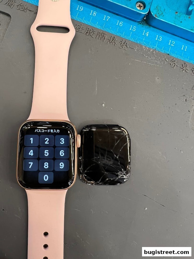 A pink Apple Watch with a cracked screen next to a working one on a repair mat.