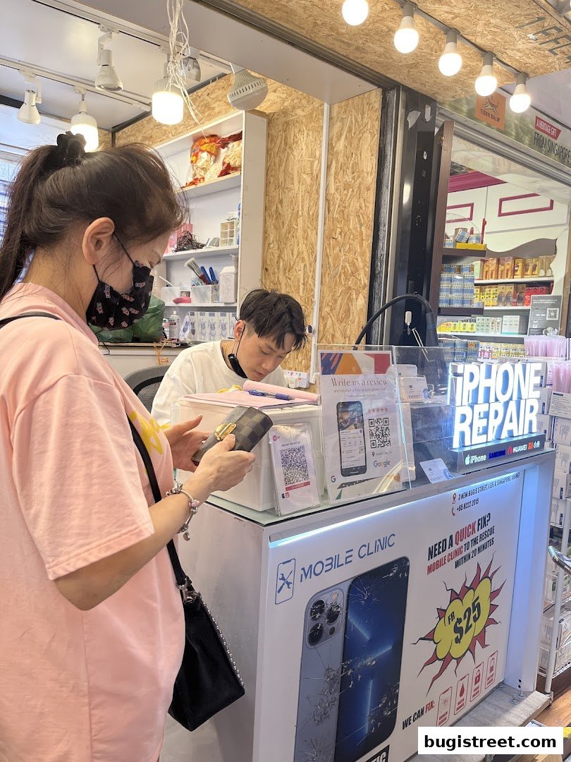 A customer is at a counter for Mobile Clinic SG, a phone repair shop.