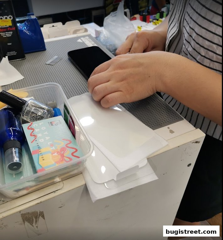 A person is applying a screen protector to a smartphone with various tools and supplies nearby.