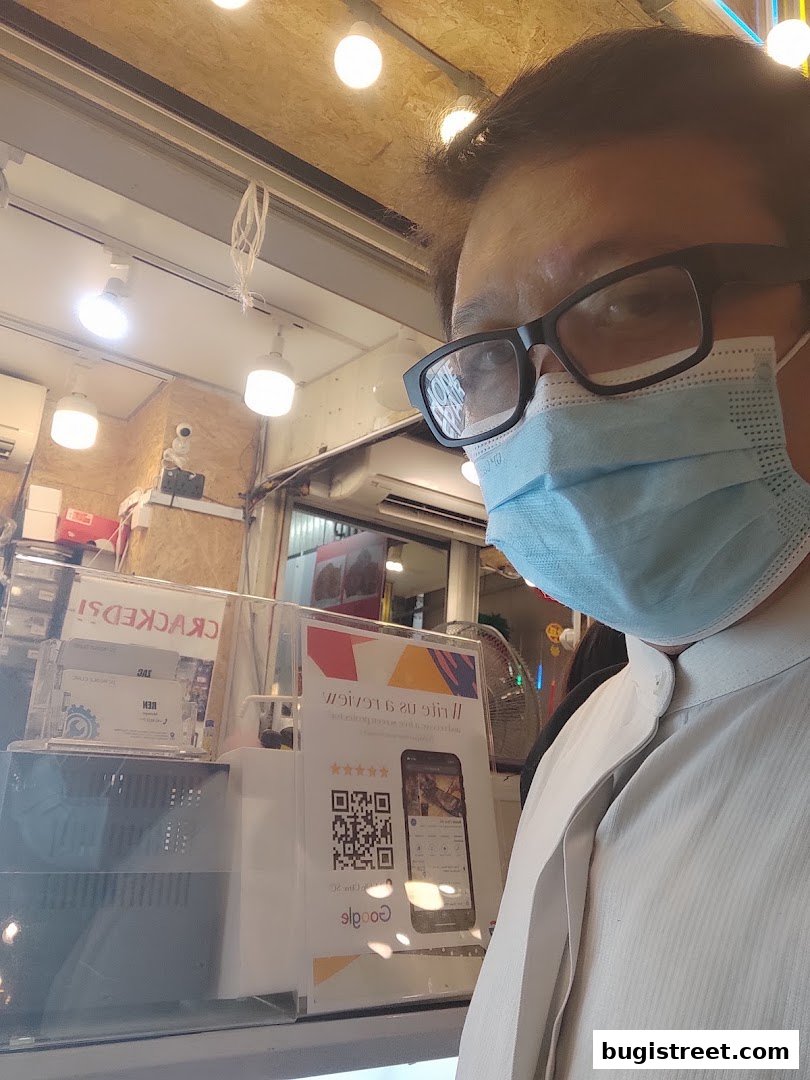A person wearing a mask and glasses is reflected in a shop window with a QR code.