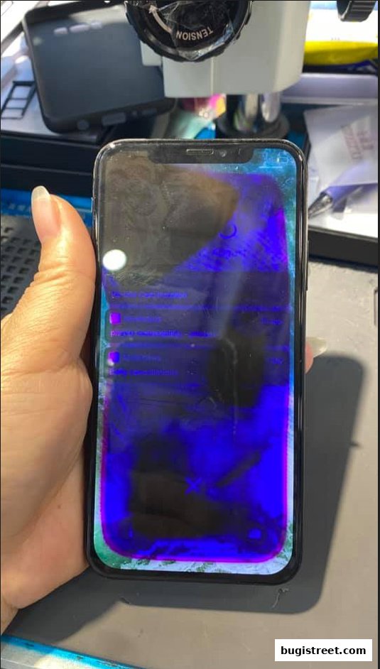 A hand holds a smartphone with a damaged screen displaying purple and blue blotches.
