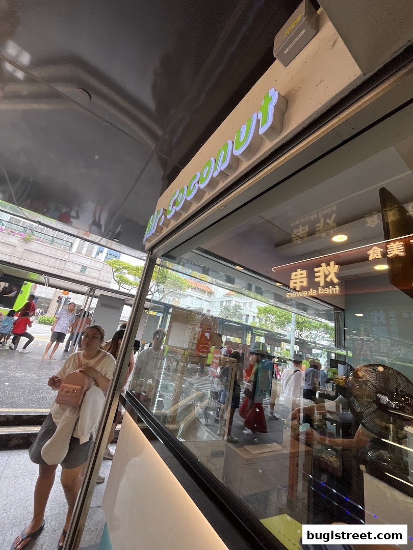 The Mr. Coconut shop front with its illuminated sign and a view of the bustling street outside.