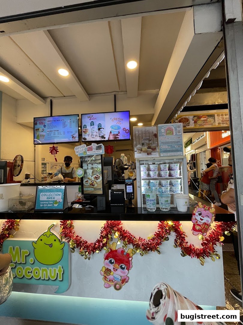 A view of the Mr. Coconut stall with a menu, drinks, and staff preparing orders.
