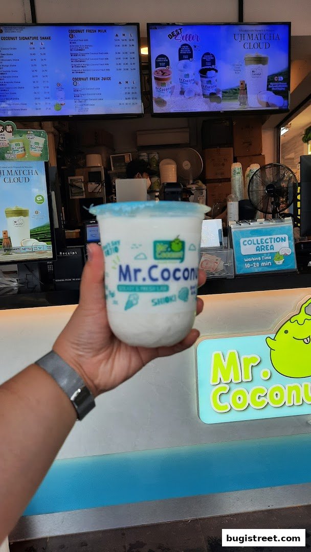A hand holds a Mr. Coconut drink in front of the shop's menu and branding.