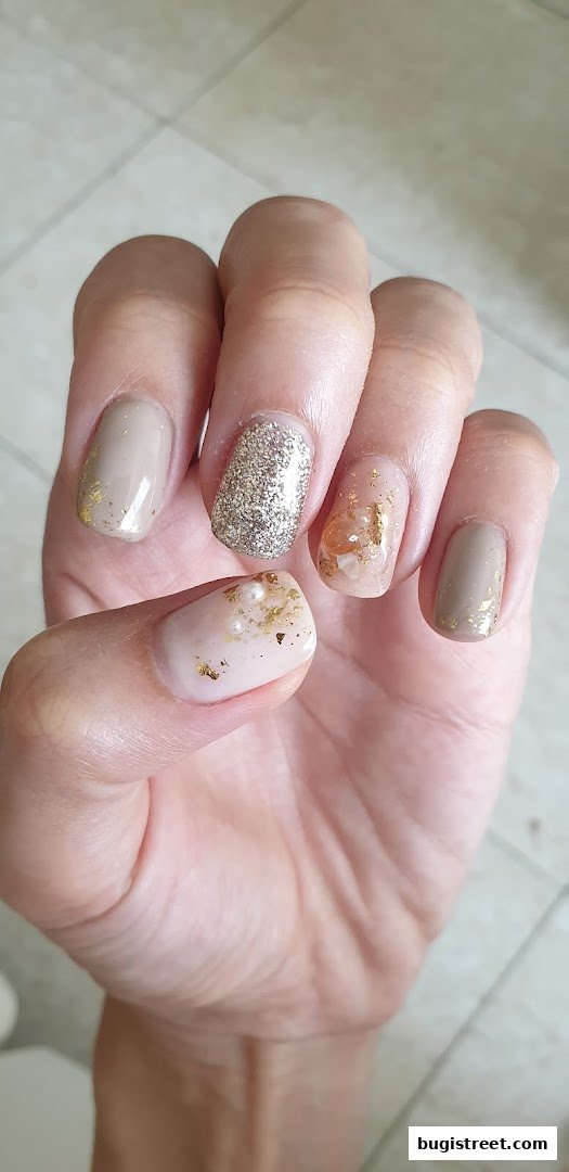 A close-up of a hand showcasing elegant nail art with beige polish, glitter, and gold accents.