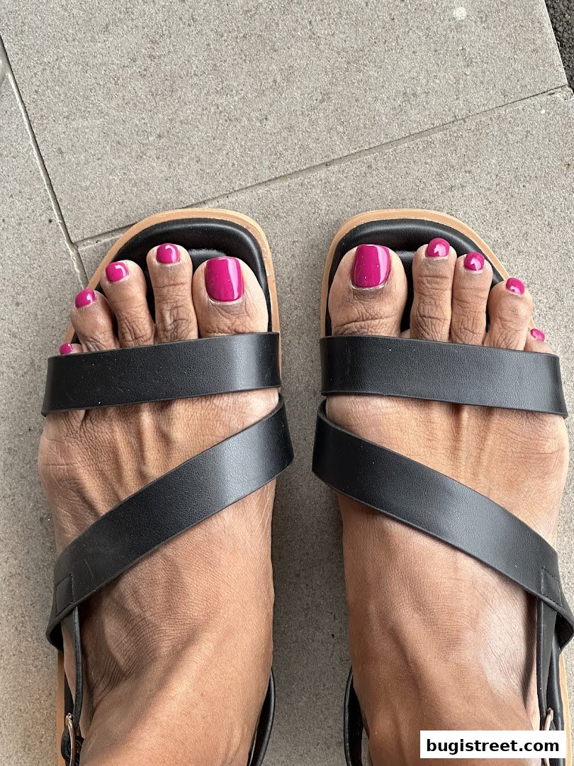 A close-up shot of feet with vibrant pink toenail polish and black sandals.