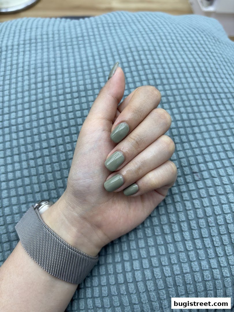 A hand with short, oval-shaped nails painted in a muted olive green color.