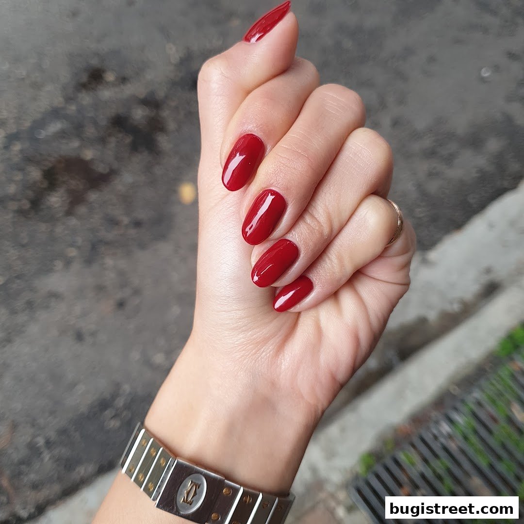 A hand with perfectly manicured, glossy red nails and a stylish watch.