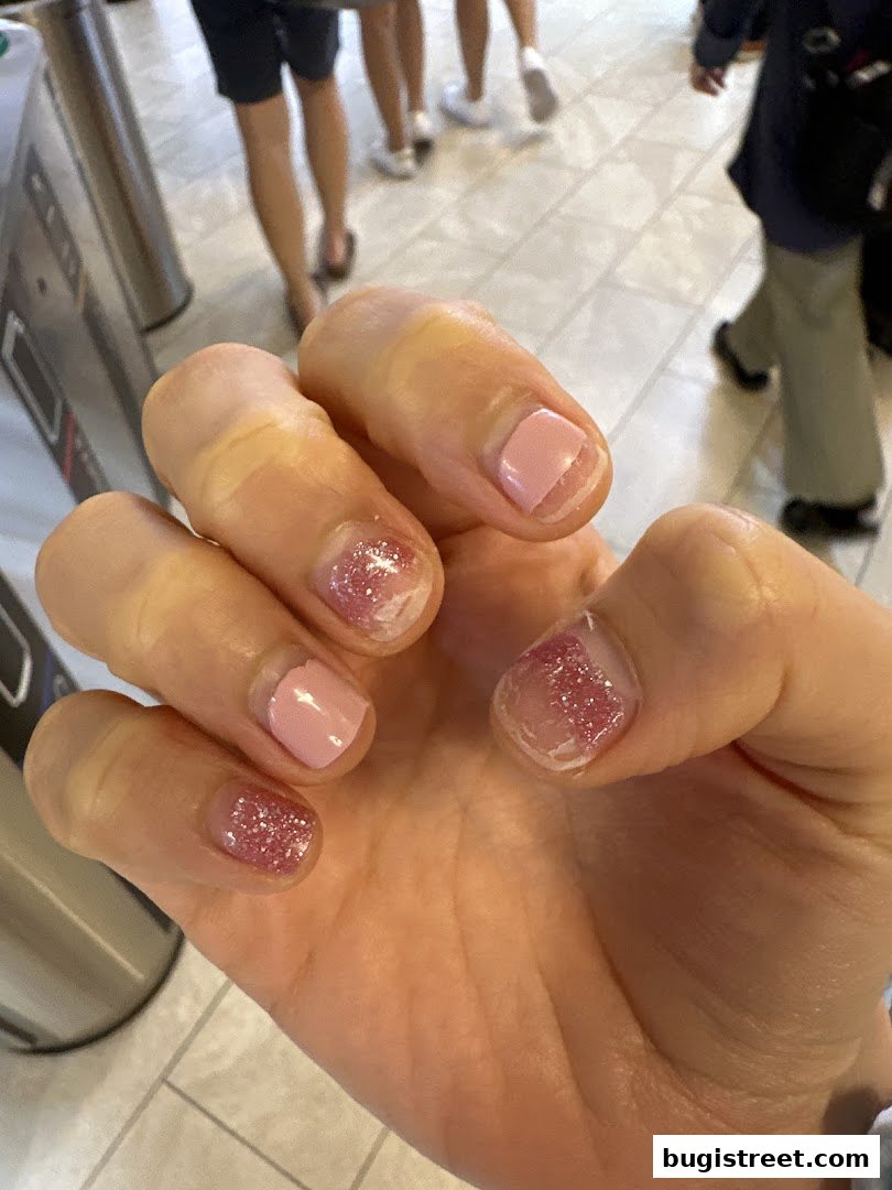 A close-up of a hand with freshly done pink and glitter nail art.