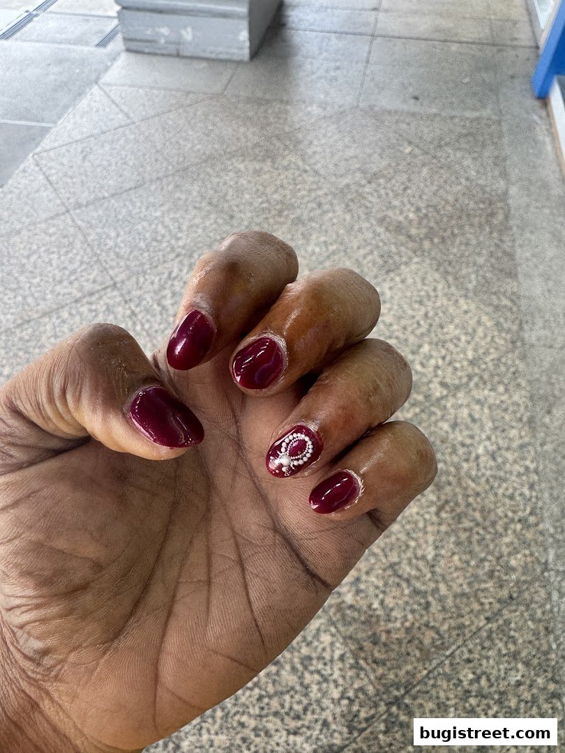 A close-up of a hand with dark red, glossy nails, one featuring intricate white nail art.