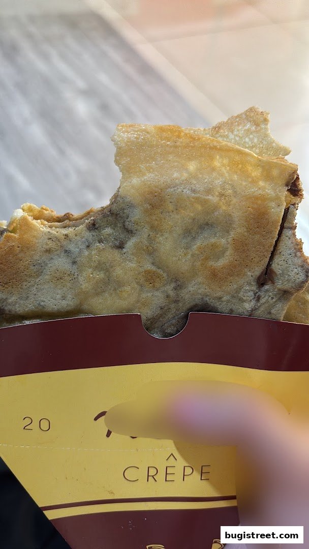 A close-up of a delicious crepe with a bite taken out, held in branded packaging.