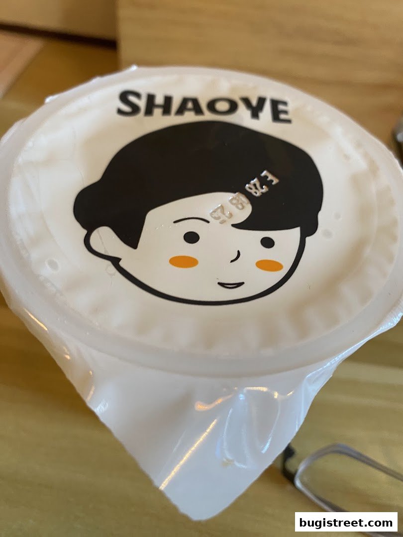 A close-up of a sealed drink cup with a cartoon face and the brand name SHAOYE.