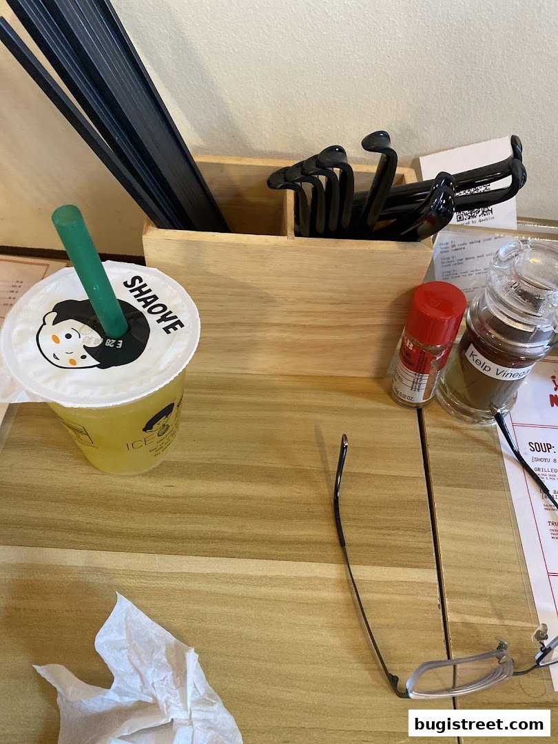 A table setting with a drink, chopsticks, and condiments at a noodle bar.