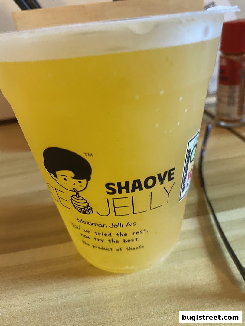 A close-up of a yellow beverage in a clear plastic cup with branding.