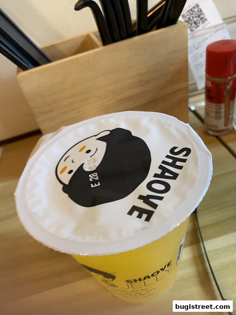 A close-up of a yellow drink with a branded lid and a wooden utensil holder.