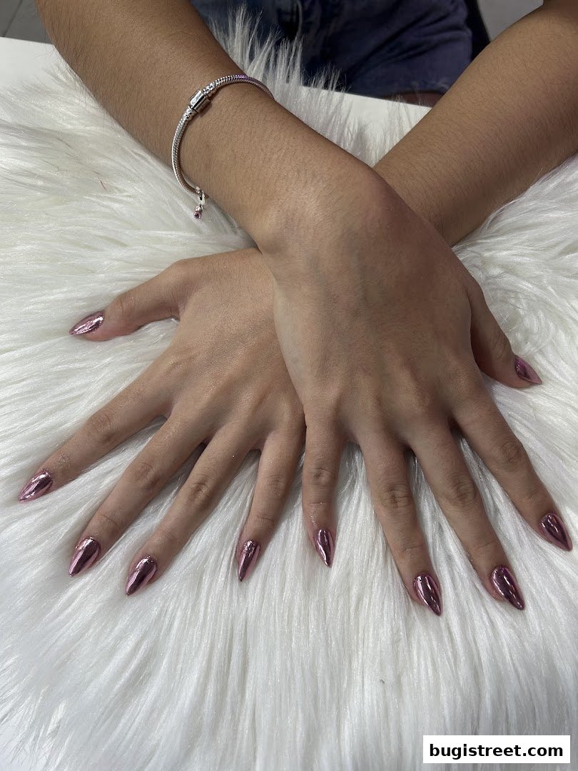 A person's hands with stiletto-shaped nails painted in a metallic rose gold polish.