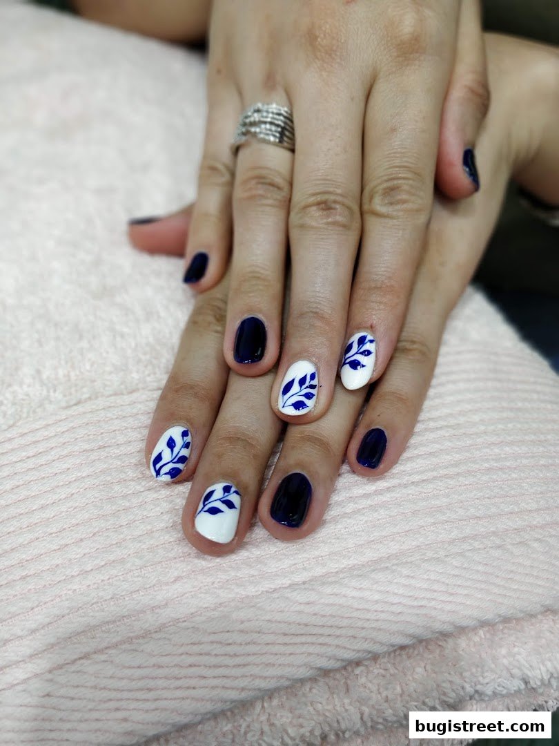 Close-up of hands with dark blue and white nails featuring blue leaf designs.