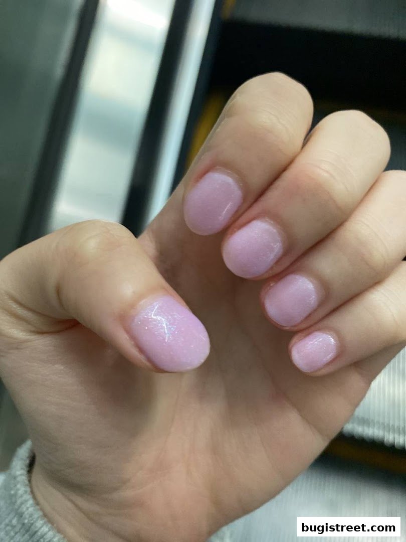 A close-up of a hand with neatly manicured light purple nails with subtle glitter.