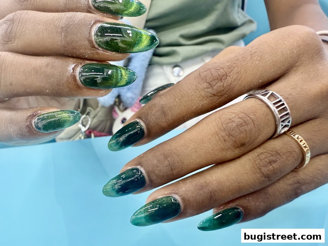 Close-up of hands with stunning green cat-eye effect gel nails and rings.