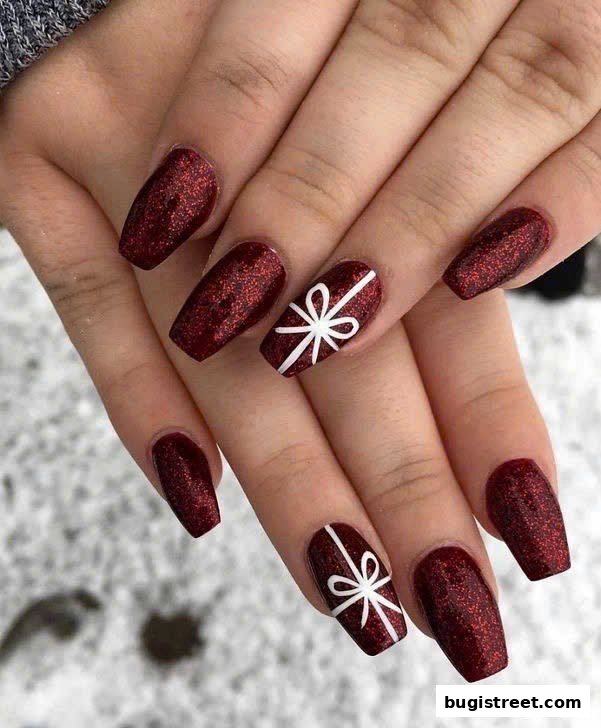 Close-up of hands with dark red glitter nails featuring white gift bow designs.