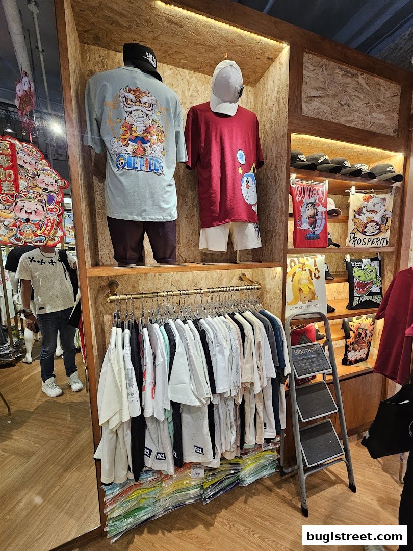 A retail shop displaying graphic t-shirts, caps, and tote bags on mannequins and racks.
