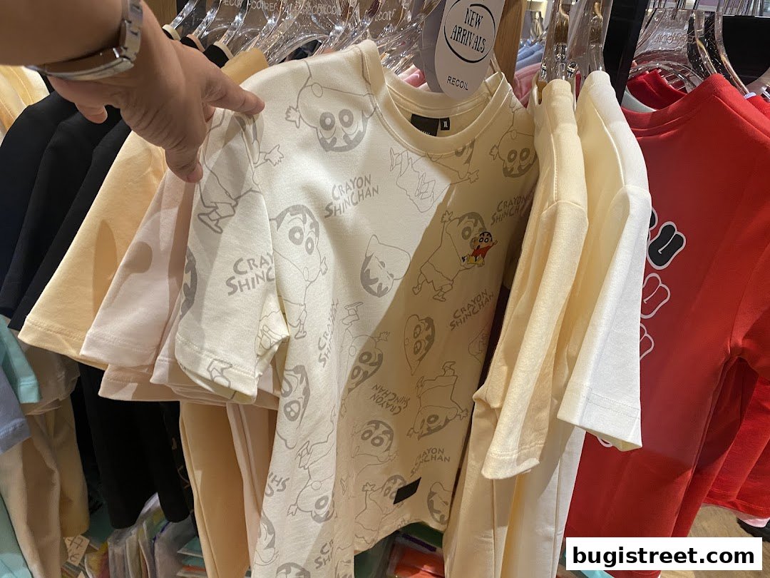 A hand points to a cream-colored t-shirt with a repeating Crayon Shin-chan pattern.