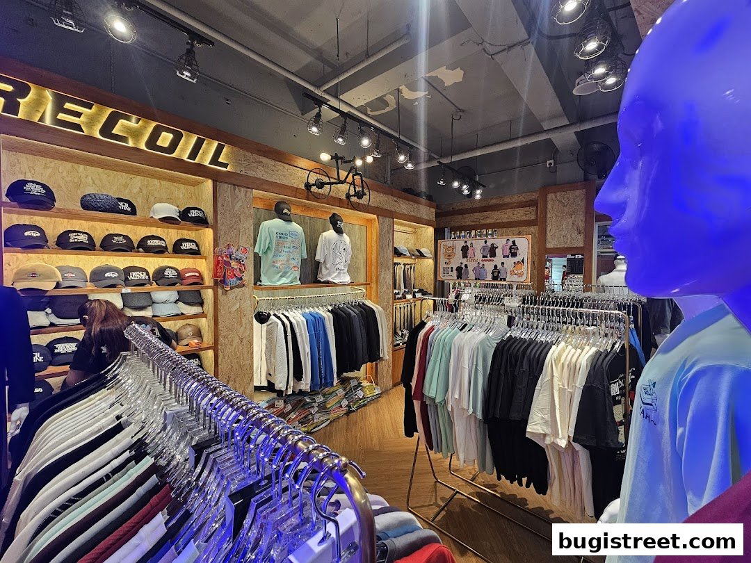 Interior of a clothing store displaying t-shirts, caps, and jackets on racks and shelves.