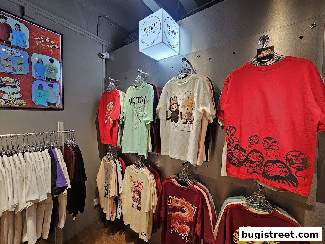 A retail shop interior displaying a variety of graphic t-shirts on hangers and a promotional poster.