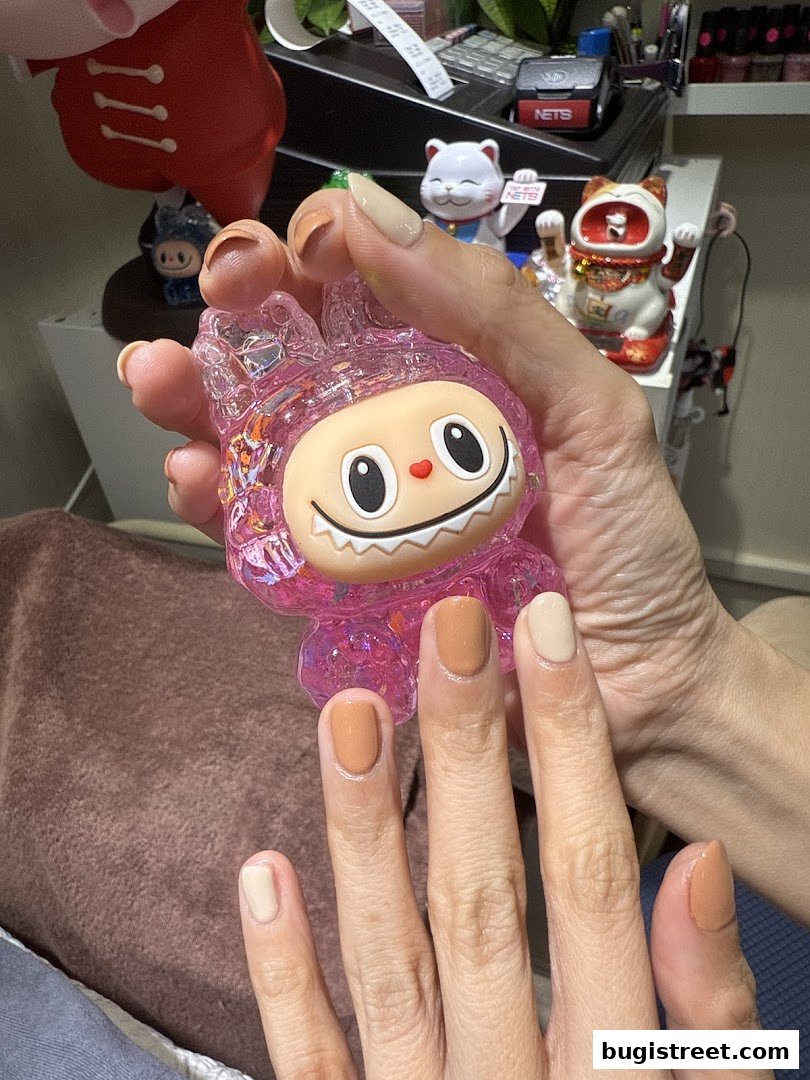 A person shows off their nails painted in various shades of brown and beige, holding a pink toy.
