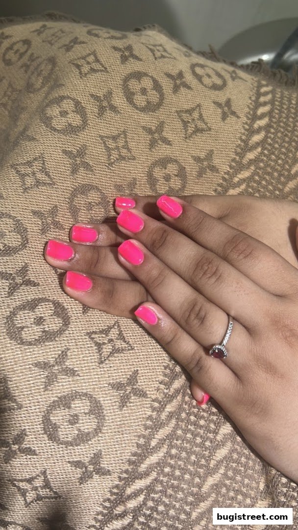A close-up of hands with vibrant pink gel nails and a diamond ring.