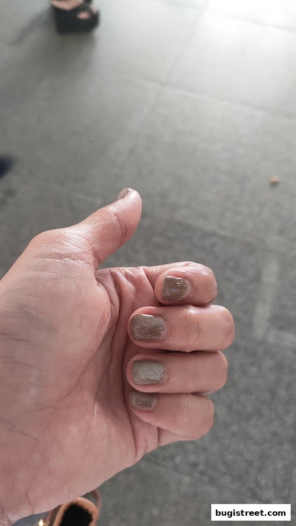 A close-up of a hand with freshly painted nails in a shimmering brown shade.