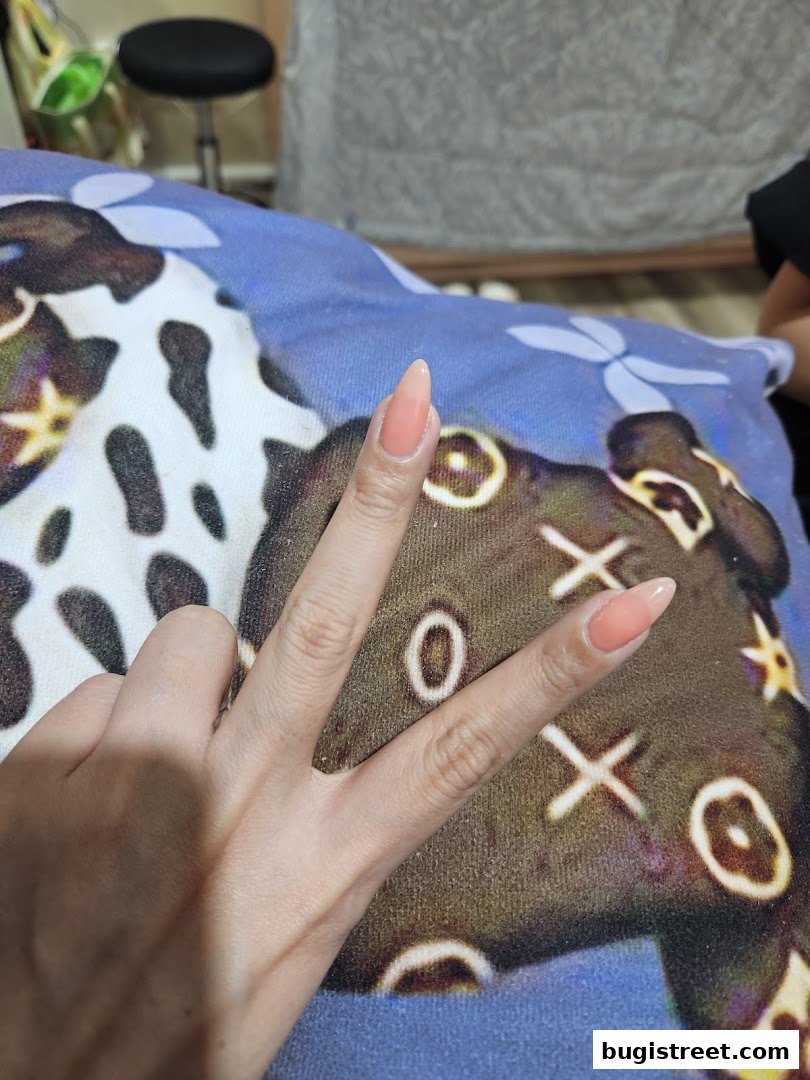 A hand with perfectly manicured peach-colored nails is shown against a patterned background.