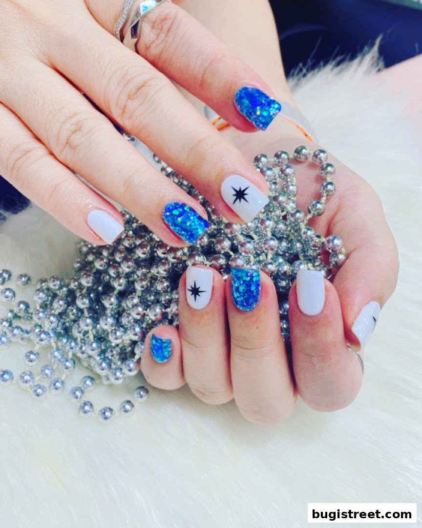 Close-up of hands with white and blue glitter nails, adorned with silver beads.