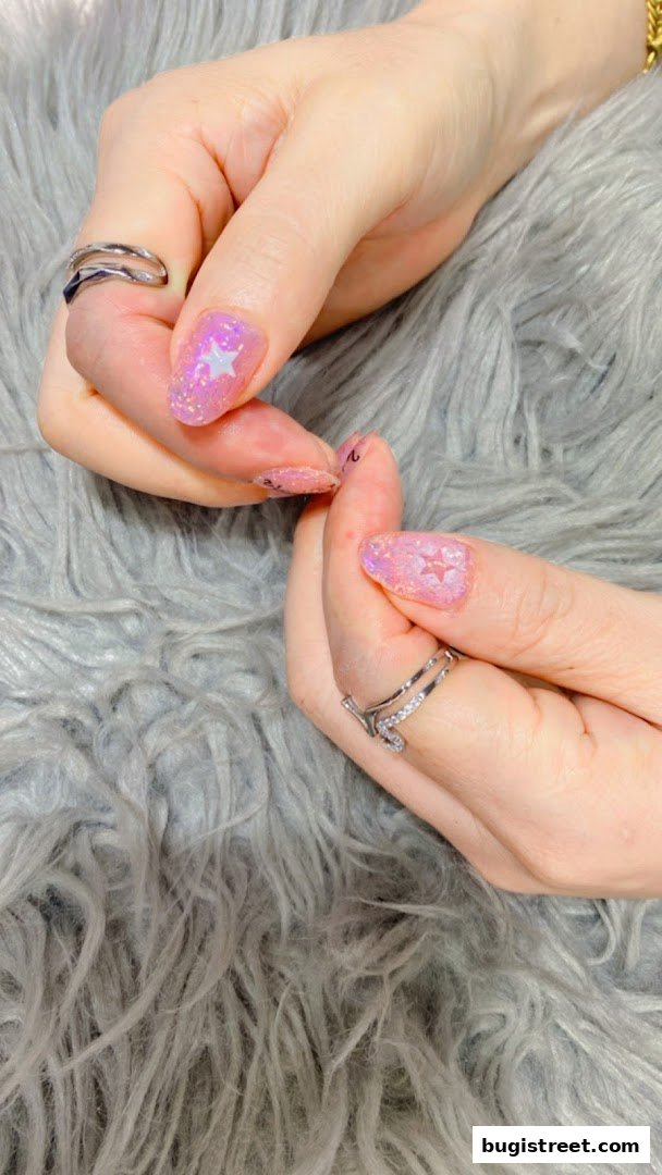 Close-up of hands with sparkling pink nails featuring star designs and rings.