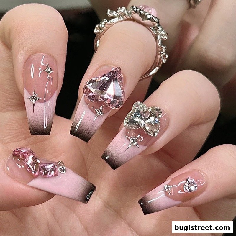 Close-up of hands with elaborate pink and black ombre coffin nails adorned with rhinestones and charms.
