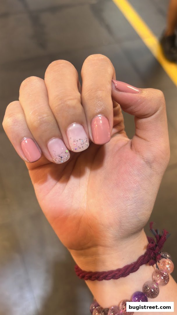 A close-up of a hand with beautifully manicured nails featuring a gradient of pink and glitter.