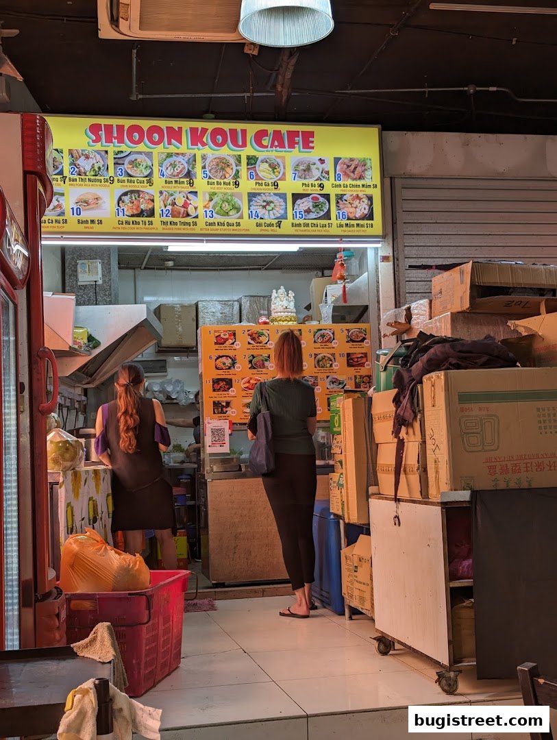 Shoon Kou Cafe displays a vibrant menu with various Vietnamese dishes and two customers browsing.