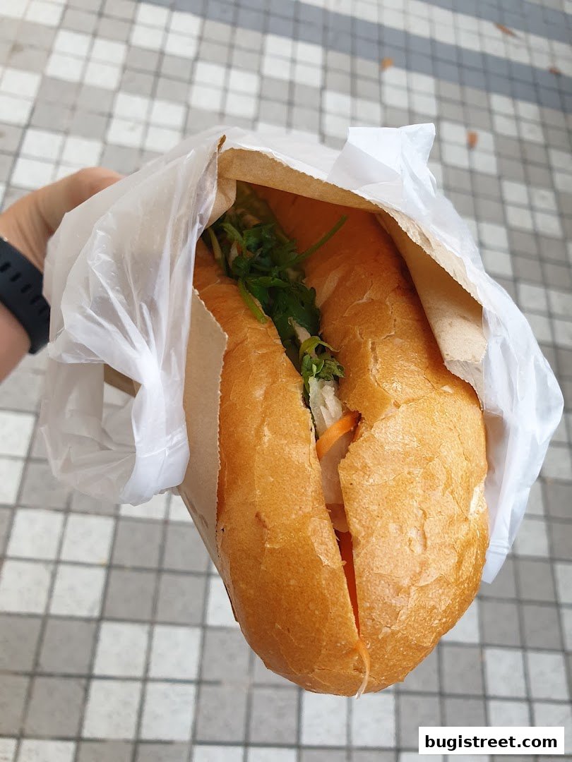 A hand holds a delicious banh mi sandwich wrapped in paper.