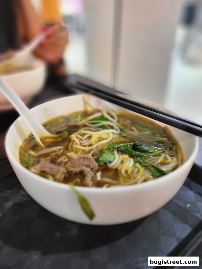 A close-up of a steaming bowl of pho with beef, noodles, and herbs, ready to be enjoyed.