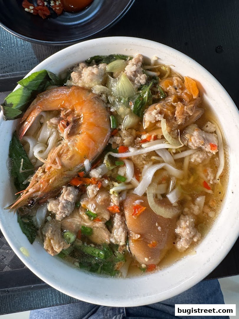 A close-up shot of a steaming bowl of noodle soup with shrimp, pork, and vegetables.