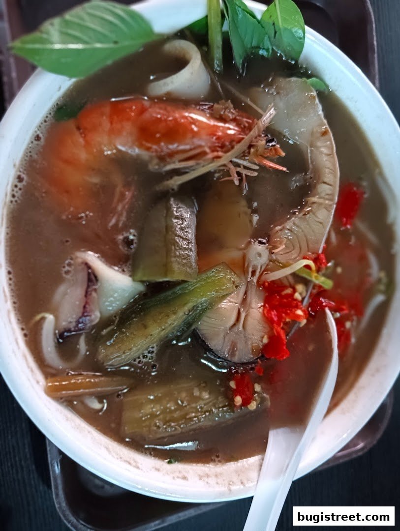 A close-up of a steaming bowl of seafood soup with shrimp, squid, and vegetables.