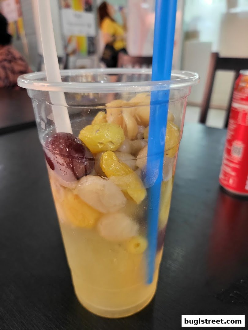 A refreshing beverage with various fruits and ice, served in a clear plastic cup with straws.