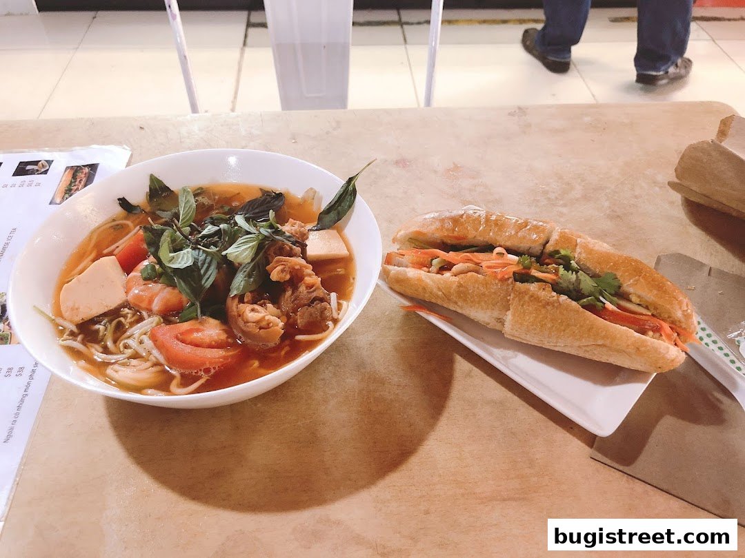 A bowl of Vietnamese noodle soup and a banh mi sandwich are displayed on a table.