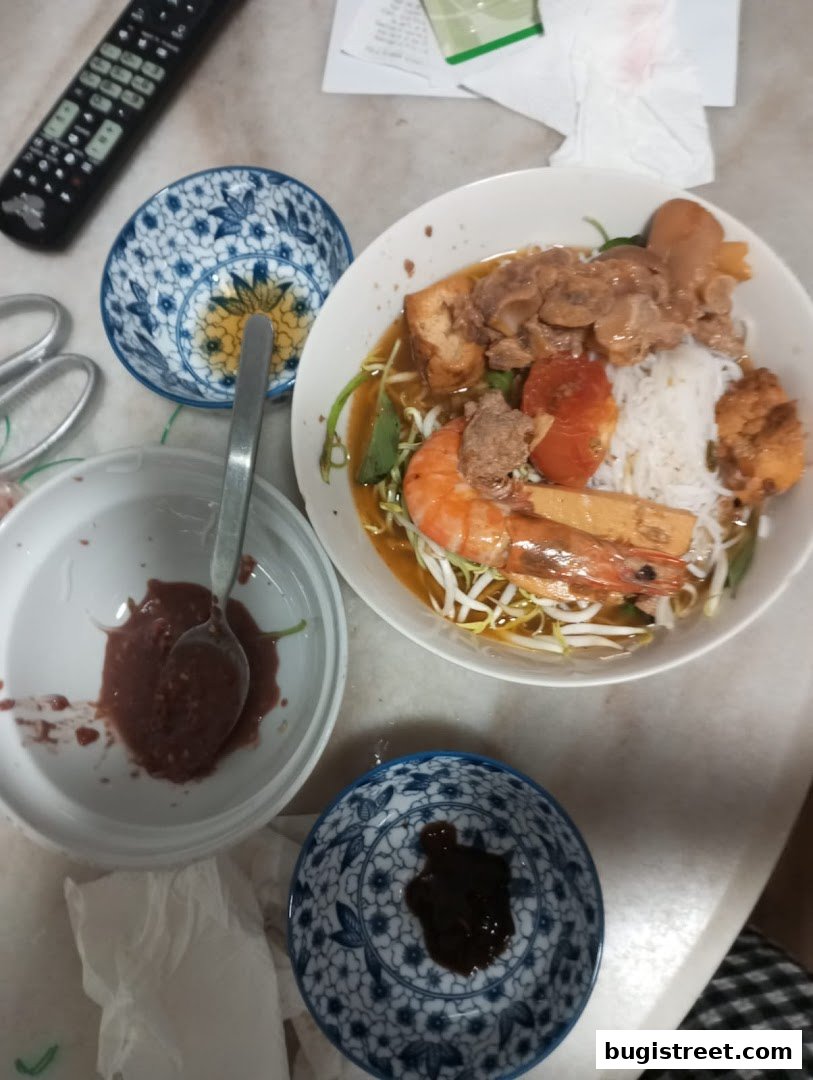 A bowl of noodle soup with shrimp, meat, tofu, and vegetables, served with side dishes.
